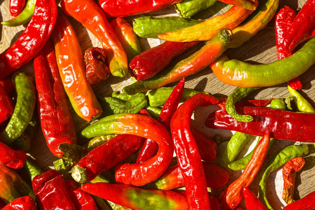 A pile of fresh red and green chillies on a wooden surface