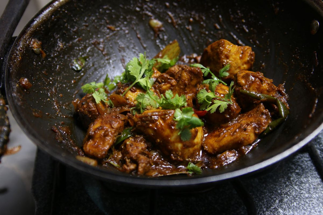 Dark pan of glossy chilli-spiced curry garnished with fresh coriander