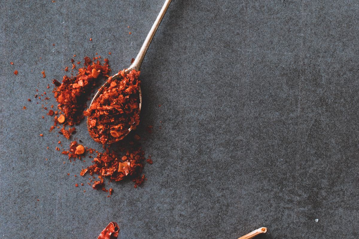 Spoonful of coarse red chilli flakes on a dark slate surface