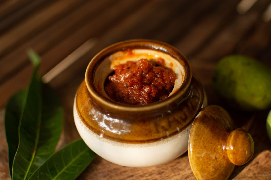 Ceramic pot of spiced achar pickle with fresh green leaves on a wooden board