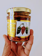 Hand holding a jar of hot pepper pickle with a visible brand label on a plain background