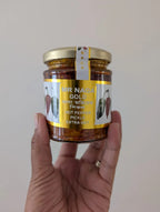Hand holding a jar of 'Mr Naga Gold' hot pepper pickle against a plain background