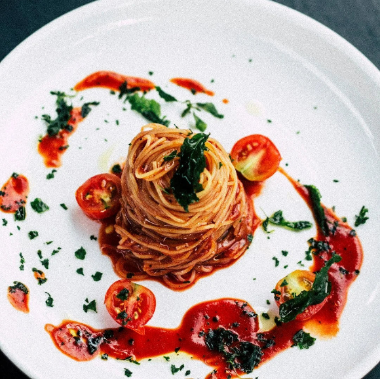 Spaghetti dish with tomato sauce and herbs on a white plate against a dark background